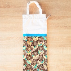 May include: A white reusable shopping bag with a brown and yellow patterned fabric lining. The fabric features a design of birds and spiderwebs. The bag has a blue trim and a small white tag with the word "Jute" printed on it.