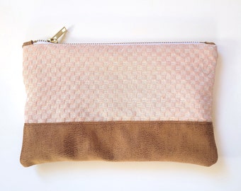 May include: A rectangular zippered pouch featuring a top section of light pink fabric with a woven basket-weave texture and a bottom section of brown faux leather with a distressed finish. The pouch includes a gold-toned metal zipper.
