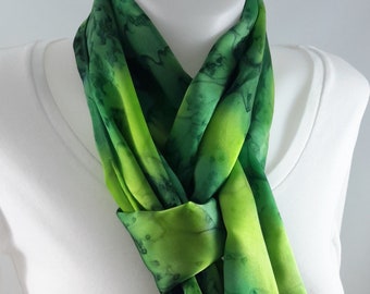 May include: A green silk scarf with a tie-dye pattern. The scarf is tied around a white mannequin's neck.