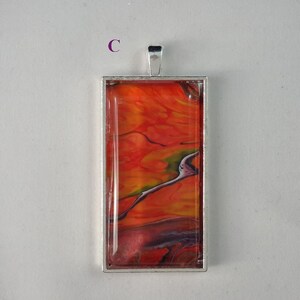 May include: A silver pendant with a rectangular glass insert featuring abstract red, orange, and yellow paint swirls.
