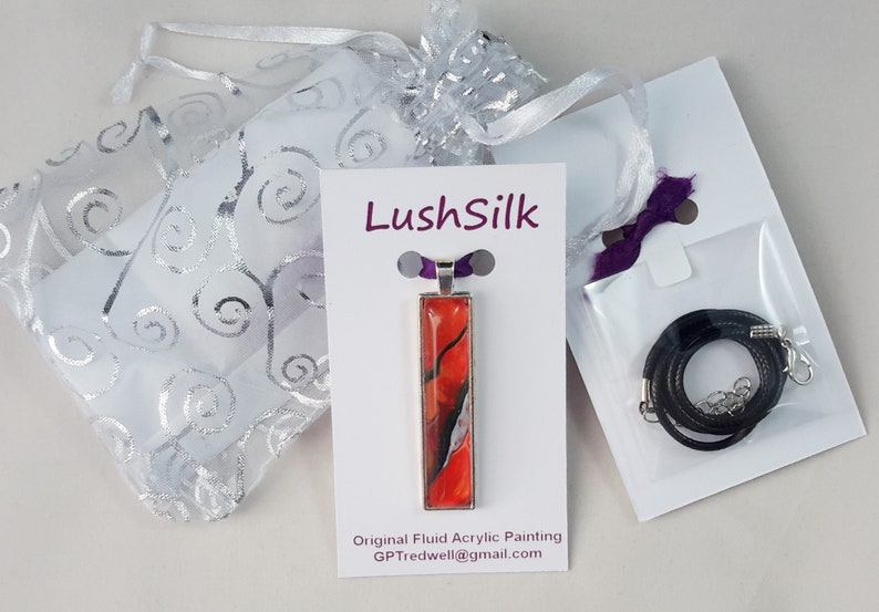 May include: A red, black, and white fluid acrylic painting on a silver pendant with a black cord necklace. The pendant is displayed on a white card with the text "LushSilk" and "Original Fluid Acrylic Painting" with an email address. The necklace is packaged in a white bag with a purple ribbon.