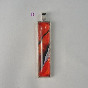 May include: A silver pendant with a rectangular glass insert featuring abstract red, orange, black, and white swirls.