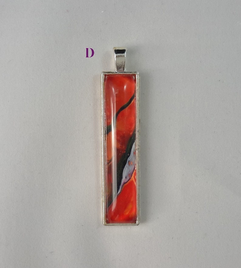 May include: A silver pendant with a rectangular glass insert featuring abstract red, orange, black, and white swirls.