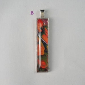 May include: A silver pendant with a rectangular glass insert featuring abstract swirls of orange, green, and black paint.