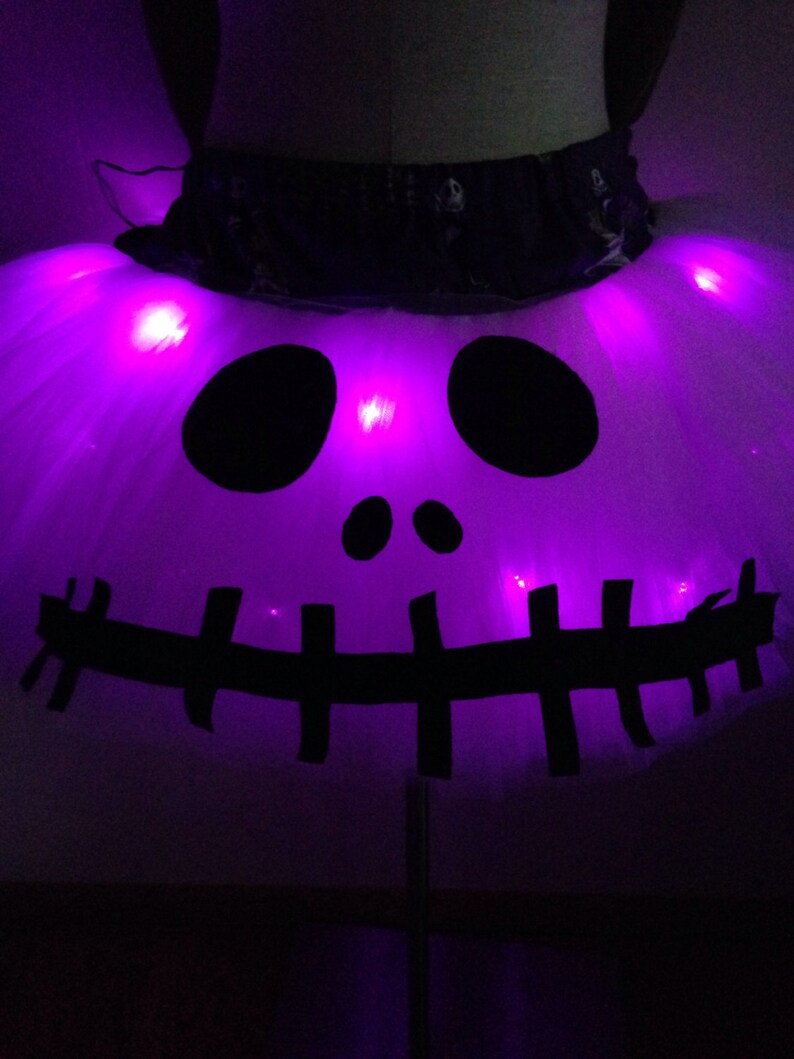 May include: A white tulle tutu skirt with a black skull and crossbones design. The skirt has purple LED lights that illuminate the design.