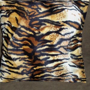 Pode incluir: Uma almofada de lançamento marrom, preta e branca com estampa de pele de tigre. A almofada é feita de um tecido macio e felpudo.