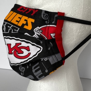 May include: Black face mask with a red, white, and yellow Kansas City Chiefs logo and musical notes. The mask has black elastic ear loops.