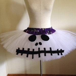 May include: White tulle tutu skirt with a black and white Jack Skellington face design. The skirt has a purple waistband.