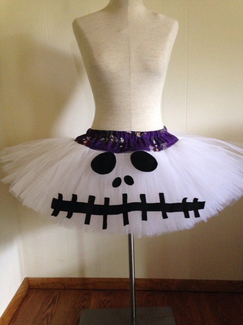 May include: White tulle tutu skirt with a black and white Jack Skellington face design. The skirt has a purple waistband.