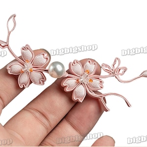 May include: Pink fabric flower hair clip with a pearl accent. The clip is shaped like a cherry blossom branch with two flowers.