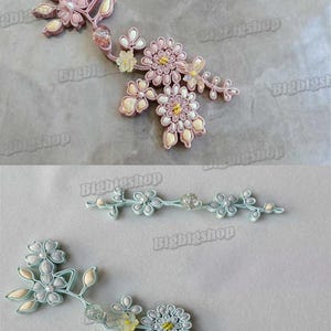 May include: Two floral embellishments are shown. One is pink with white and yellow details, the other is light blue with white and yellow details. They have a delicate, handcrafted look, ideal for craft projects.