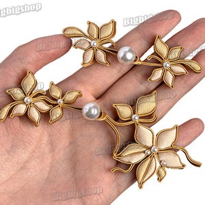 May include: Gold-toned floral hair accessories with pearl accents. Each piece features stylized flowers with cream-colored petals and a central pearl. The design is intricate and elegant, suitable for special occasions.