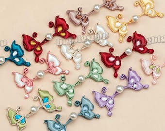 Op de afbeelding: Assortiment van 18 kleurrijke vlinder-vormige stoffen versieringen met parel accenten. Elke vlinder is gemaakt van satijnen lint en heeft een parel in het midden. De vlinders zijn in verschillende kleuren, waaronder rood, blauw, groen, paars, roze en wit.