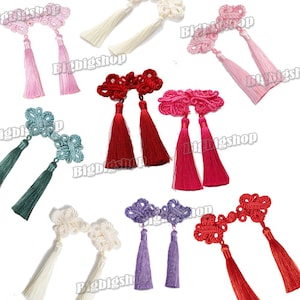 Pode incluir: Uma coleção de borlas decorativas de nós chineses em várias cores, incluindo rosa, vermelho, verde e roxo. Cada borla apresenta um design de nó na parte superior com borlas longas e fluidas. A imagem é tirada de cima.