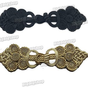 May include: Two decorative frog closures. One is black, the other is gold. Each closure features looped and coiled rope elements, connected by a braided section and a central loop.