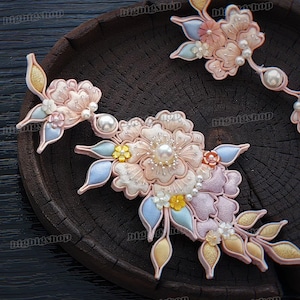 Puede incluir: Un conjunto de tres pinzas para el pelo de flores de tela rosa y azul con detalles de perlas. Las flores están dispuestas en cascada y están sujetas a una pinza de metal.