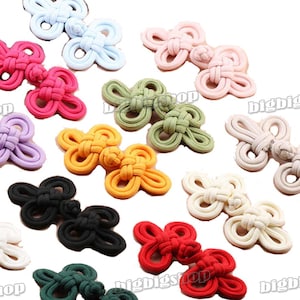 Könnte beinhalten: Sortiment von 14 bunten Stoffknöpfen mit chinesischen Knoten. Die Knoten sind in verschiedenen Farben, darunter Rot, Rosa, Grün, Blau, Gelb und Weiß. Die Knoten sind alle im gleichen Stil, mit einem Doppelknoten in der Mitte und vier Schlaufen, die sich vom Knoten aus erstrecken.