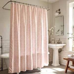 May include: A pink shower curtain with a white geometric pattern hangs in a bathroom. The curtain is suspended from a curved metal rod. The bathroom has a white sink, mirror, and a wooden bench.