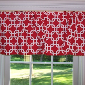 May include: Red and white geometric patterned valance with white trim. The valance is hung on a white curtain rod with white finials.
