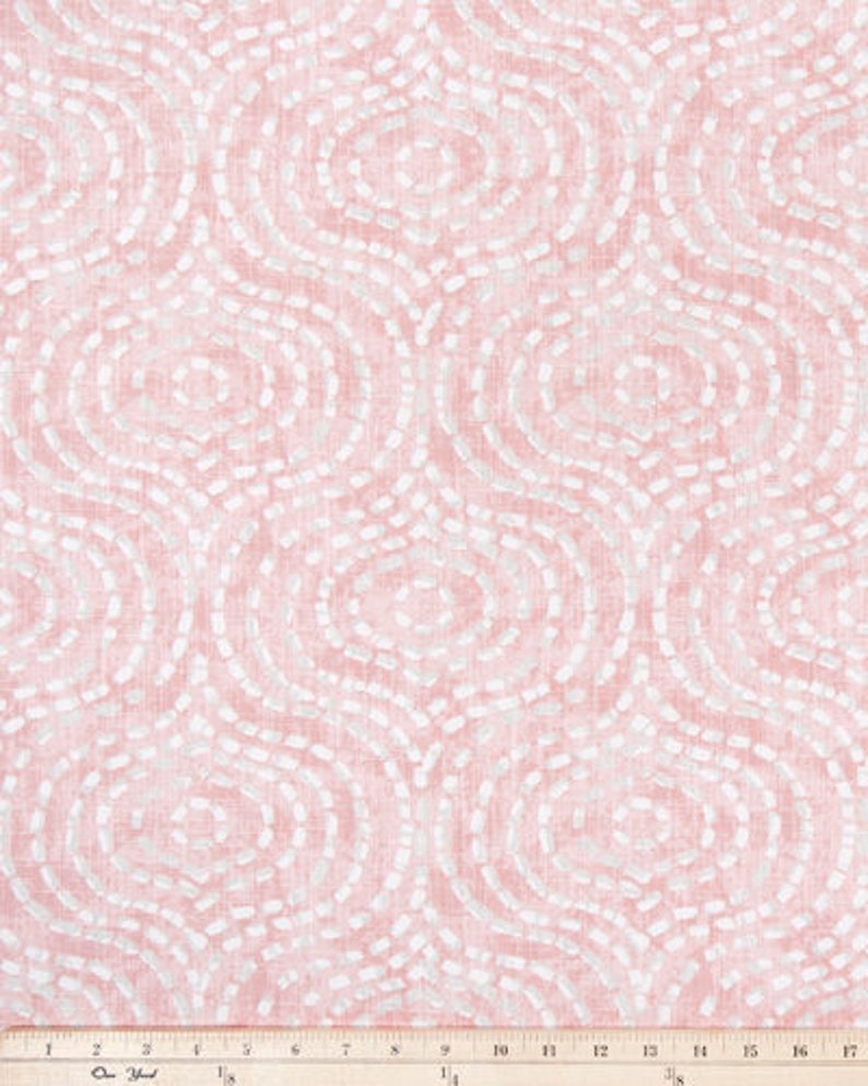 May include: Pink fabric with a repeating pattern of white, dotted, oval shapes. The fabric has a textured appearance and a ruler is at the bottom, measuring in inches. The design is reminiscent of an abstract, organic motif.