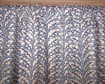 May include: A gathered curtain panel featuring a repeating botanical pattern of dark blue oak leaves on a light blue background. The fabric has a visible woven texture and is suspended from a rod, creating vertical folds across the entire surface.