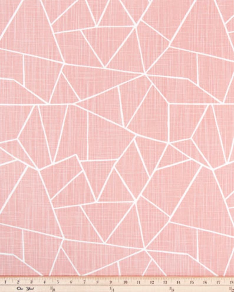 May include: A close-up of a fabric with a geometric pattern. The fabric has a light pink background with a white, linear design of irregular shapes. The fabric is textured and appears to be cotton or linen. The pattern is consistent across the fabric.
