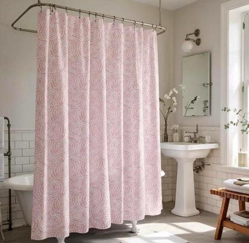 May include: A pink and white patterned shower curtain hangs in a bathroom. The curtain features a repeating circular design. The bathroom has a white pedestal sink, a mirror, and a bathtub.