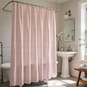 May include: A pink shower curtain with a white geometric pattern hangs from a curved metal rod. The curtain is the focal point of a bathroom scene, with a white pedestal sink, a clawfoot tub, and a wooden stool visible.