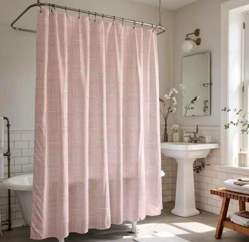 May include: A pink shower curtain with a white geometric pattern hangs from a curved metal rod. The curtain is the focal point of a bathroom scene, with a white pedestal sink, a clawfoot tub, and a wooden stool visible.