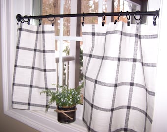 May include: Black and white checkered cafe curtains hanging on a black metal curtain rod. The curtains are made of a lightweight fabric and are perfect for adding a touch of farmhouse style to any kitchen or dining room.