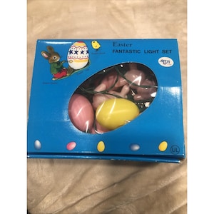 Puede incluir: Una caja azul con un juego de luces «Easter Fantastic». El juego incluye luces rosas con forma de conejito y huevo, y una luz amarilla con forma de huevo. La caja tiene ilustraciones de un conejito de Pascua, un huevo de Pascua y un pollito.