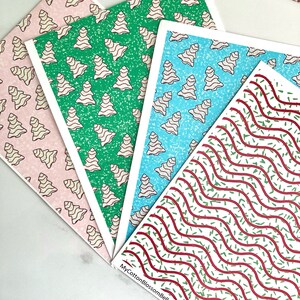 May include: Four sheets of wrapping paper with different Christmas patterns. One sheet has a pink background with white gingerbread trees, another has a green background with white gingerbread trees, another has a blue background with white gingerbread trees, and the last sheet has a white background with red and green wavy lines.