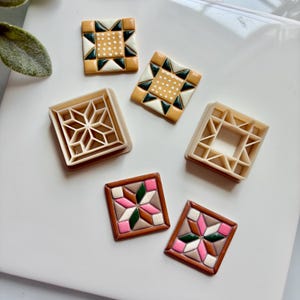 May include: A collection of square cookie cutters and corresponding square cookies. Two beige plastic cutters feature geometric star patterns. Four cookies display intricate quilt-inspired designs in shades of mustard yellow, dark green, white, pink, and brown.