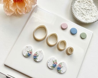May include: A set of polymer clay earring making tools and supplies. The tools include a set of four round cutters and a set of four small round cutters. The supplies include two pairs of polymer clay earrings with a floral design. The earrings are on a white surface.