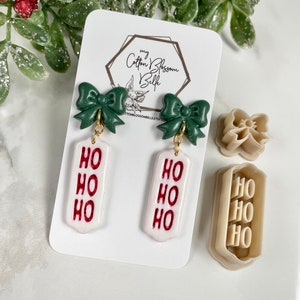May include: Green bow earrings with a white tag that says "HO HO HO" in red lettering. The earrings are displayed on a white card with the shop name "my Cotton Blossom Belle".