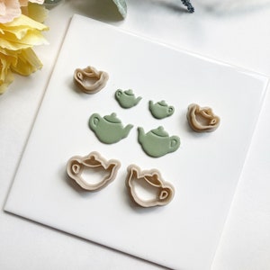 May include: A set of seven teapot cookie cutters in two sizes and two colors. The cutters are made of plastic and are in the shape of a teapot. There are four green teapots and three brown teapots.