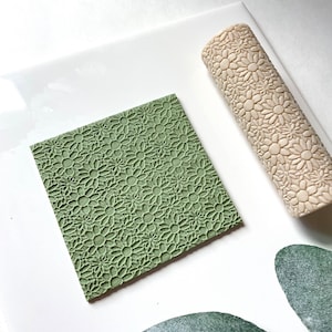 May include: A green and white rolling pin with a daisy pattern. The rolling pin is used to create a textured surface on fondant or clay.