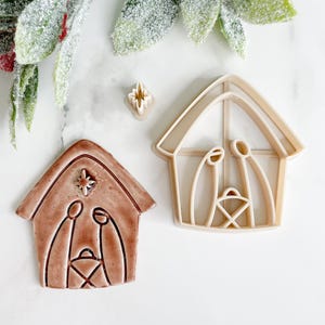 May include: A set of three brown plastic cookie cutters shaped like a nativity scene. The cutters include a star, a manger, and a stable.