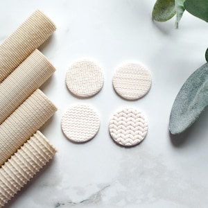 May include: An overhead shot displays four small, textured, off-white circular objects and four rolled beige mats. The circular objects have different patterns: dot, weave, chevron, and knit. The mats have a ribbed texture.