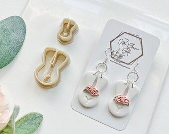 May include: White ceramic bunny earrings with pink flowers and silver hoops. The earrings are displayed on a white card with the text "my Cotton Blossom Belle" and a website address.