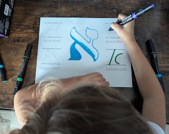 May include: A child practices writing the Hebrew letter 'aleph' in different styles. The worksheet includes 'book print', 'Torah script', 'block print', and 'cursive script' headings. The child is using blue, green, and purple markers.