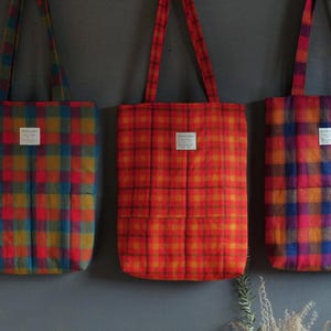May include: Three tote bags with plaid patterns in shades of red, orange, blue, and green. The bags have a quilted design and are made of a soft, textured fabric.