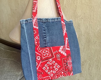 May include: A blue denim tote bag with red and white bandana fabric accents. The bag has two long straps and a large main compartment.