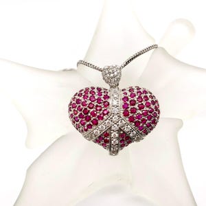 May include: A heart-shaped pendant necklace with a silver chain. The pendant is encrusted with small, round, deep red gemstones and white diamonds. The pendant has a peace sign design.