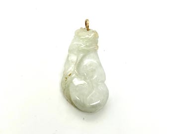 May include: A carved jade pendant with a gold-colored bail. The pendant is a pale green color with a smooth, polished surface. The jade is carved with a detailed, organic design.
