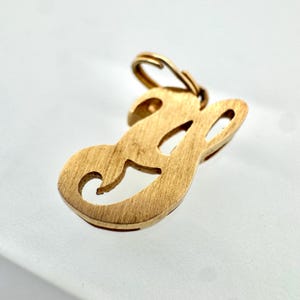 Puede incluir: Colgante dorado con forma de la letra "E". El colgante tiene un acabado cepillado y un pequeño lazo en la parte superior para una cadena. La letra está estilizada con un diseño curvo.