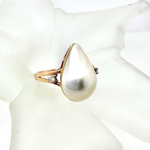 May include: A gold ring featuring a large, pear-shaped pearl. The ring has a split shank design with small accent stones on either side of the pearl. The pearl has a lustrous, creamy white color.