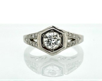 May include: A silver ring with a round, clear diamond set in a hexagonal bezel. The band is decorated with smaller diamonds.