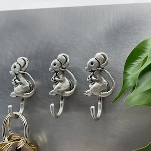 May include: Three silver mouse-shaped hooks with a key ring hanging on one of the hooks.