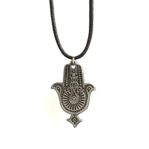 May include: A silver hamsa hand charm necklace with a black cord. The hamsa hand is a symbol of protection and good luck.